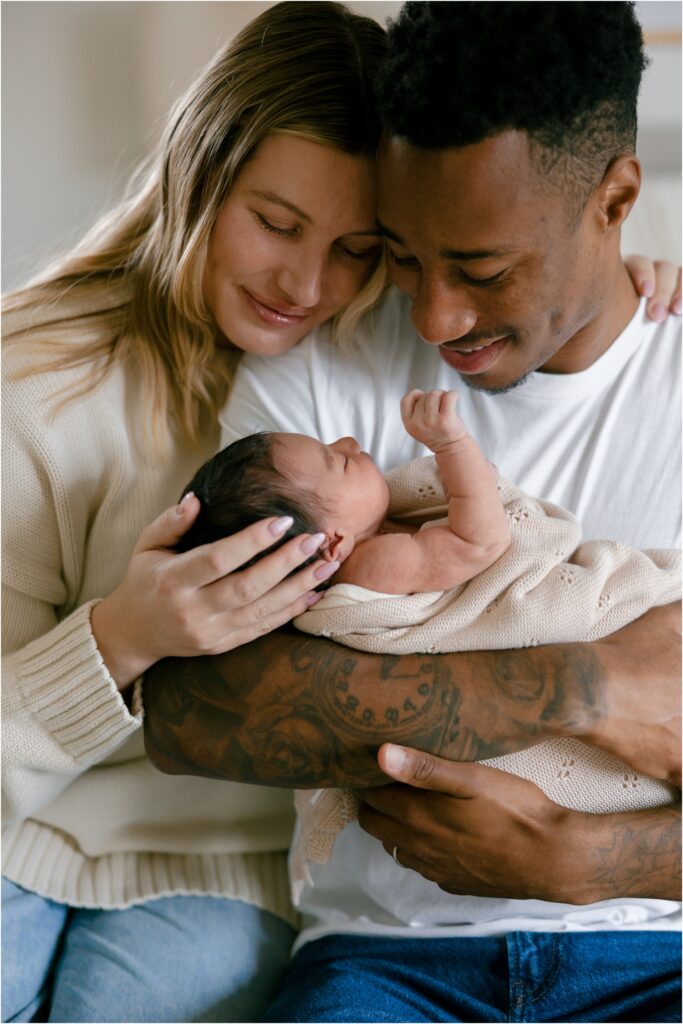 Parents holding their newborn baby, smiling and looking at the infant.